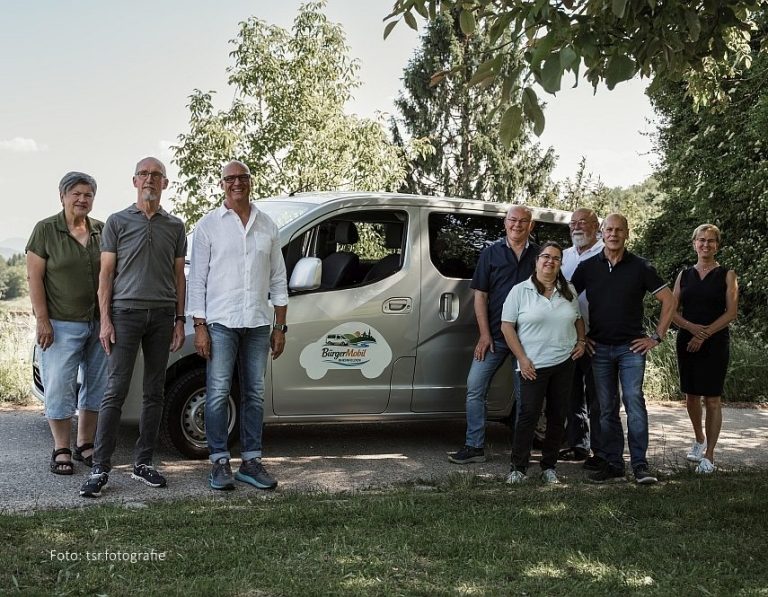 Gruppe von acht Personen neben dem BürgerMobil Van in einem grünen Außenbereich.